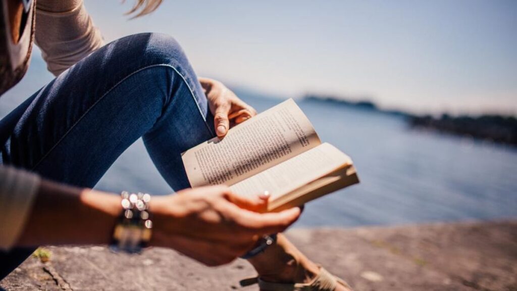 Person relaxing in a cozy chair while reading a book by a window