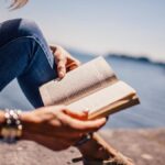 Person relaxing in a cozy chair while reading a book by a window